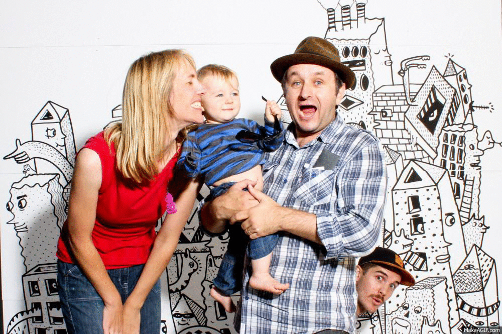 Artist hides behind couple with baby as they pose in front of BMD mural at Big Day Dowse in Lower Hutt
