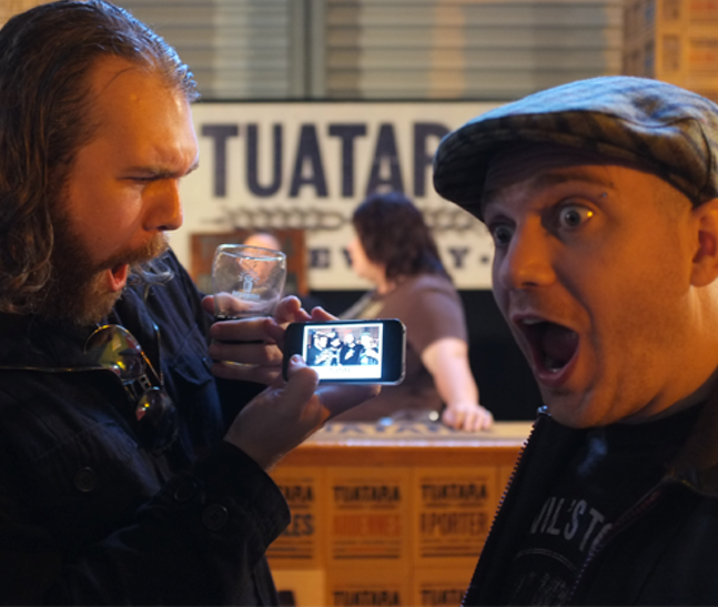 Two men at Beervana in Wellington hold up their portable device, exclaining that it amazing